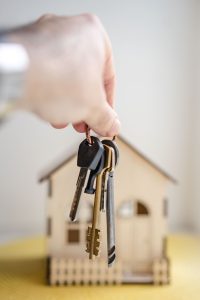 Crop faceless real estate agent with keys from new house bought with mortgage against wooden model of building